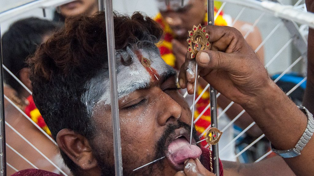 Durchstoßen der Zunge mit einem Metallstab als Vorbereitung für Thaipusam in Singapur